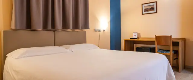 Una camera matrimoniale: il letto bianco, la scrivania di legno e la tenda