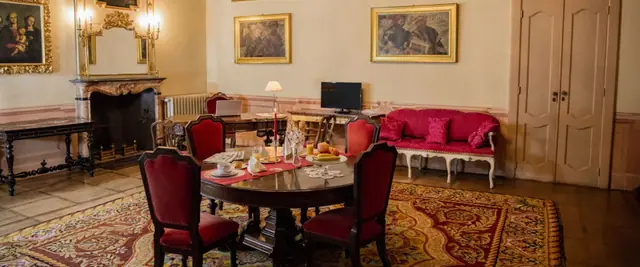 Il salotto della suite «Villa Antica», al piano nobile: le sedie rosse attorno al tavolo, il camino e i quadri alle pareti